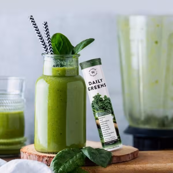 Wellbeing Nutrition Daily Greens effervescent tablets tube next to a glass of green smoothie