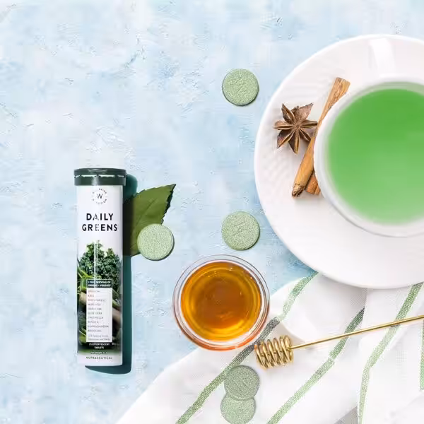 Tube of Wellbeing Nutrition Daily Greens effervescent tablets next to a prepared green drink, honey, and spices