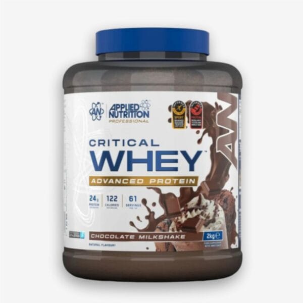 The image displays a large dark gray tub of Applied Nutrition Critical Whey Advanced Protein powder with a blue lid, featuring a label that depicts a chocolate milkshake with splashing liquid and chocolate chunks.