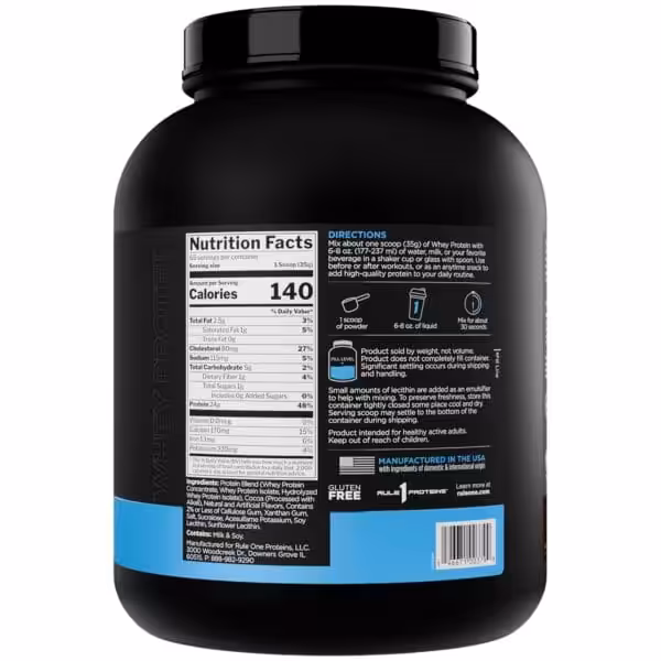 A black container of whey protein powder with a prominent label displaying nutrition facts, directions, and ingredients is visible against a white background.