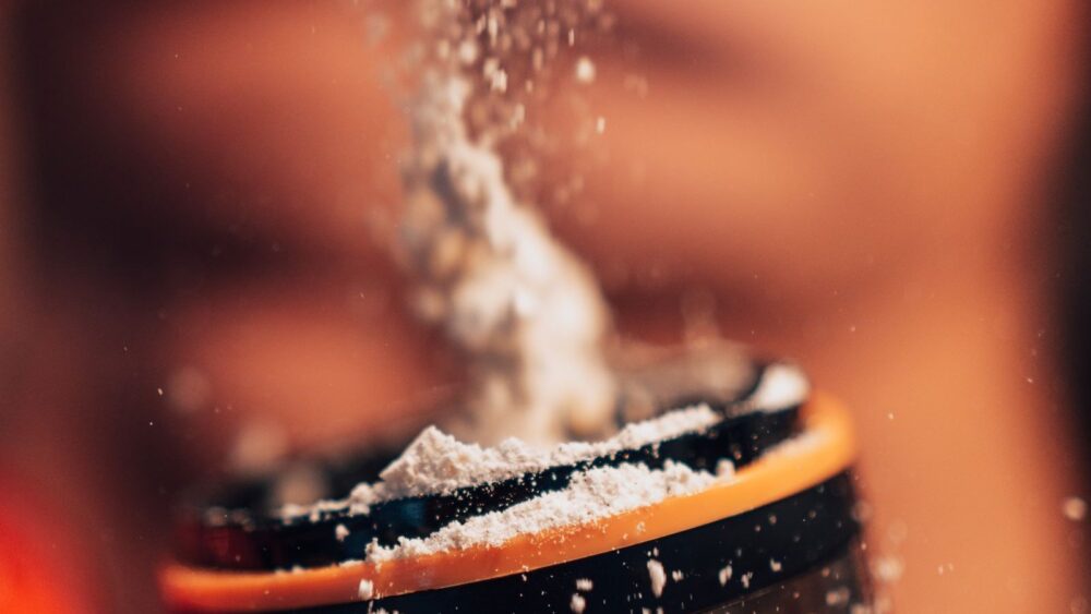 Hydrolyzed whey protein powder being poured into a shaker bottle